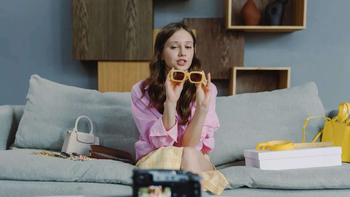 Woman holding sunglasses with shopping items and filming setup
