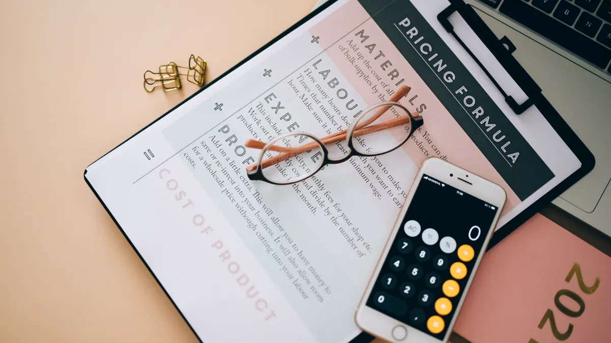 Clipboard with pricing formula sheet beside a phone and laptop