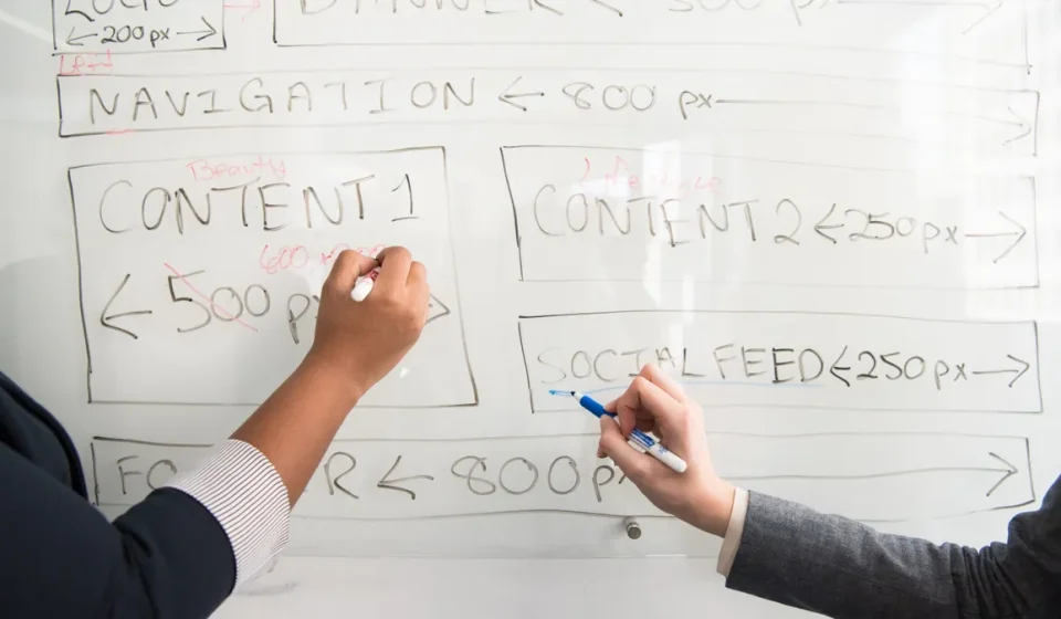 hands sketching a website wireframe on a whiteboard